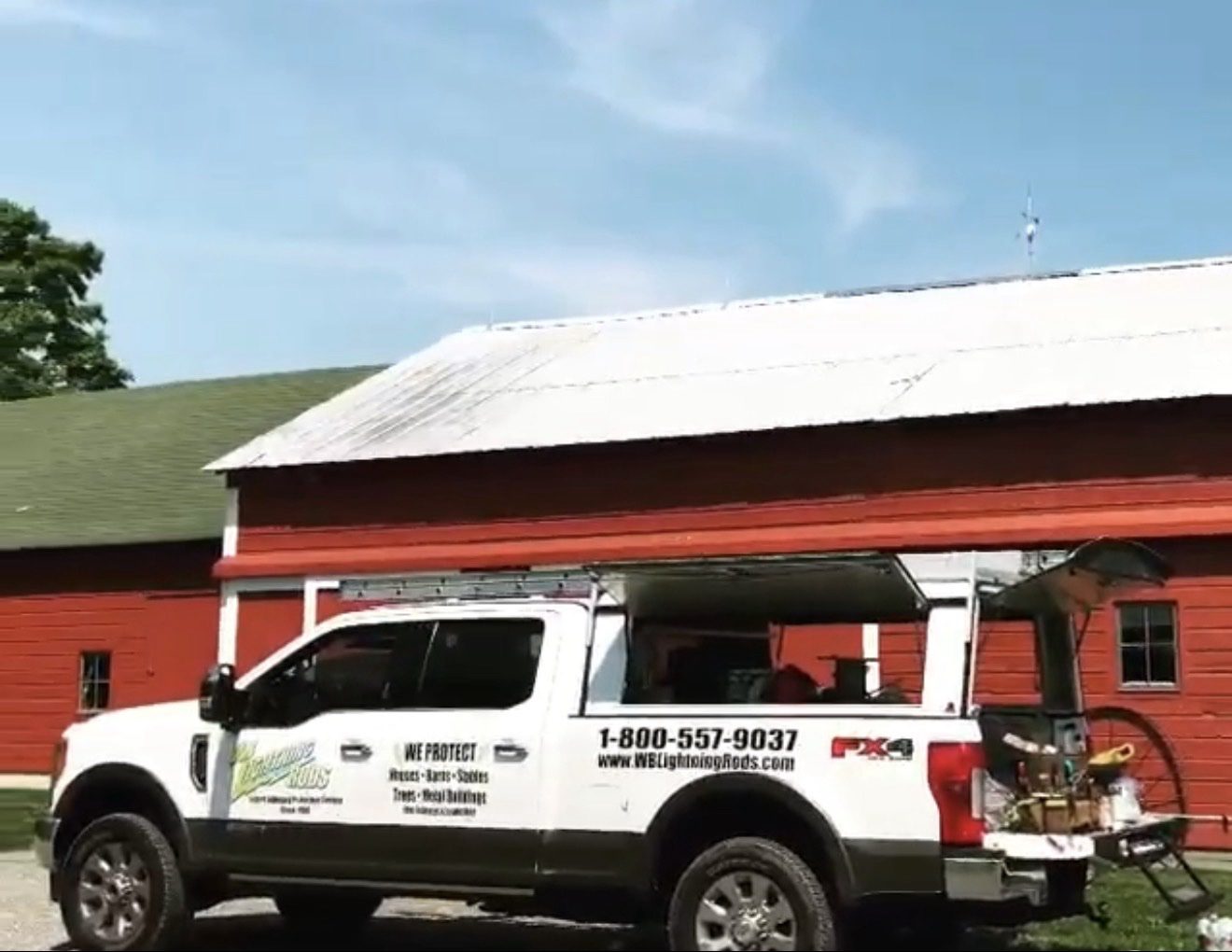 WB Lightning Rods work truck parked in front of red farm barns on a dairy farm